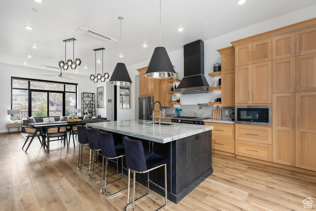 Kitchen featuring built in microwave, wall chimney exhaust hood, a sink, light wood finished floors, and recessed lighting