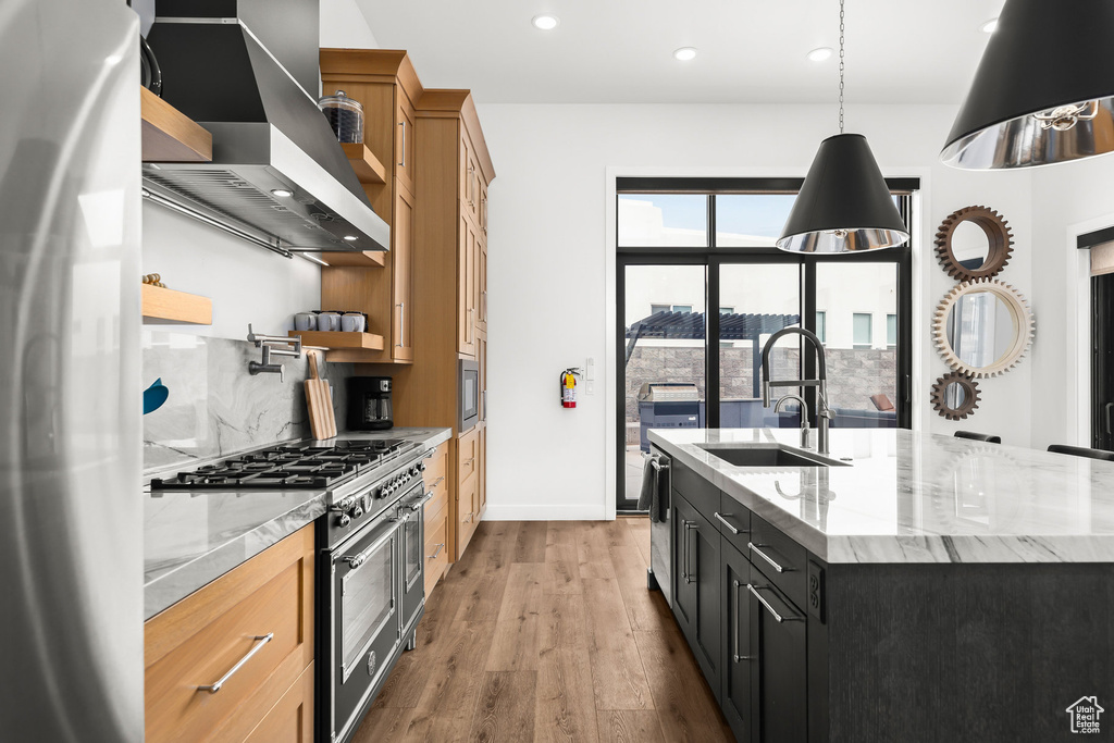Kitchen with appliances with stainless steel finishes, a sink, wall chimney exhaust hood, wood finished floors, and recessed lighting