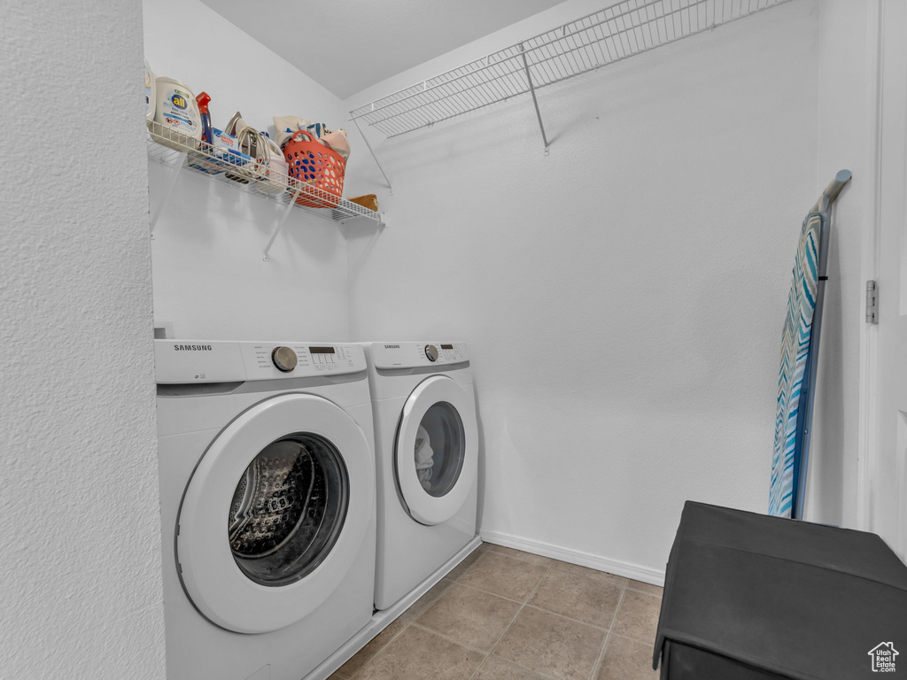 Clothes washing area featuring washer and clothes dryer, laundry area, baseboards, and light tile patterned floors