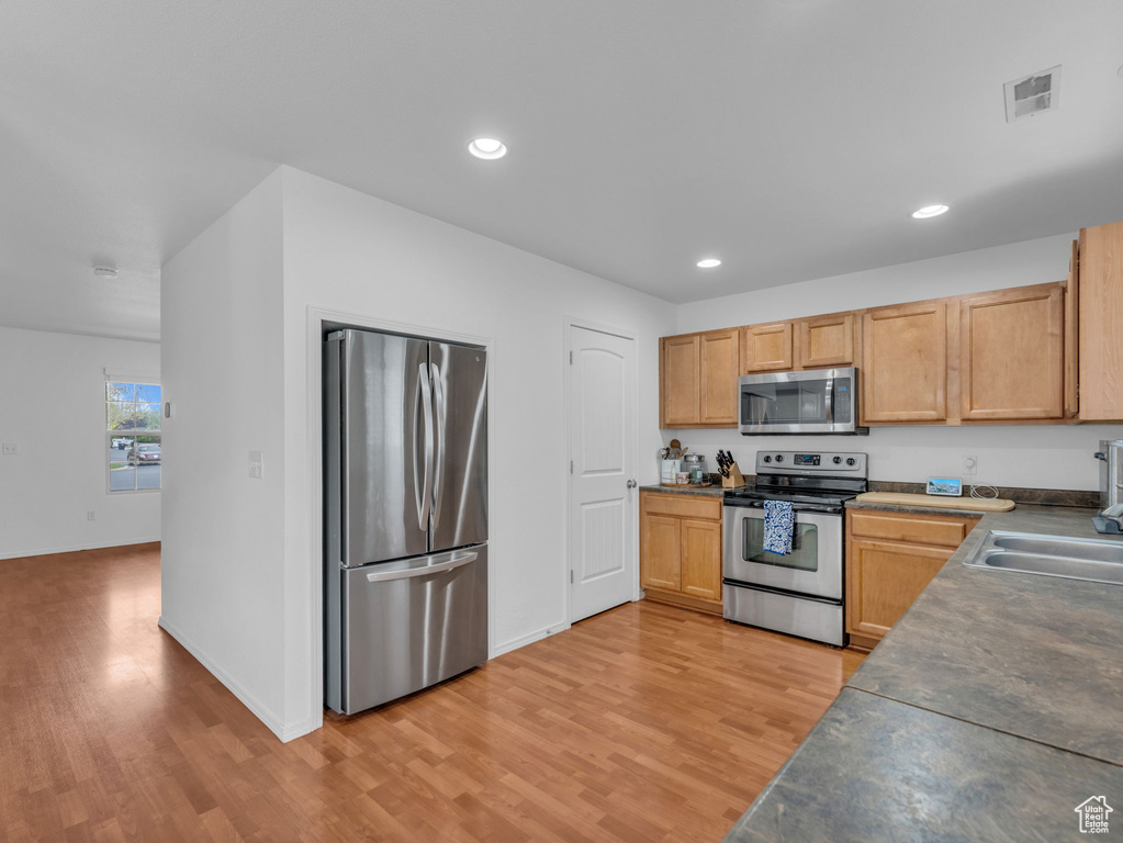 Kitchen featuring stainless steel appliances, visible vents, recessed lighting, light wood finished floors, and dark countertops