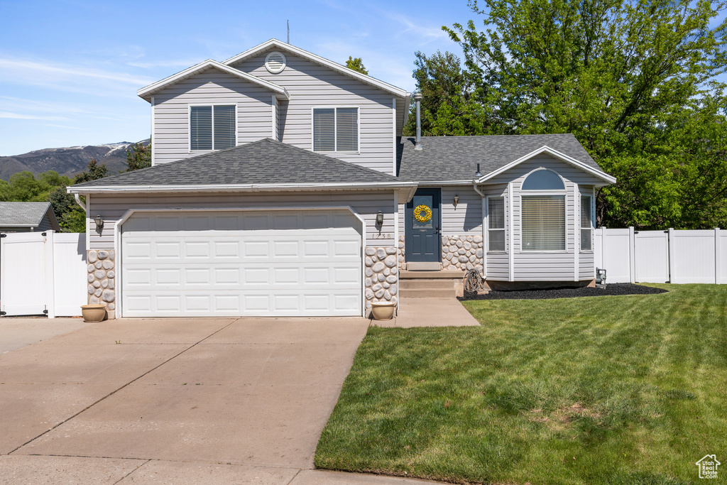 View of front facade featuring concrete driveway, roof with shingles, an attached garage, and stone siding