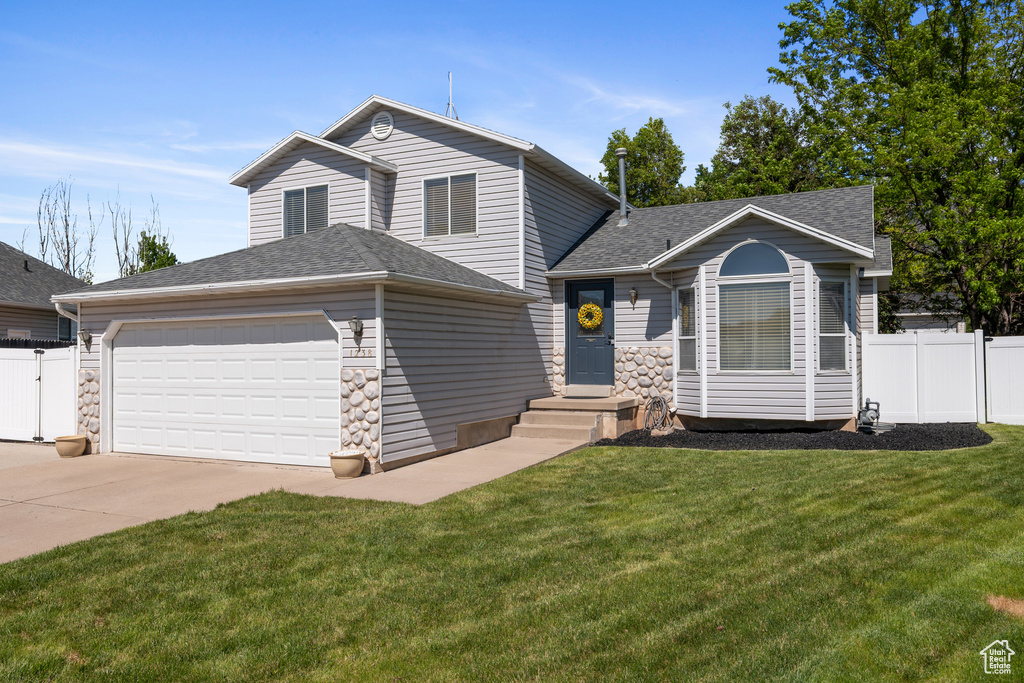 Tri-level home with concrete driveway, an attached garage, a shingled roof, and stone siding