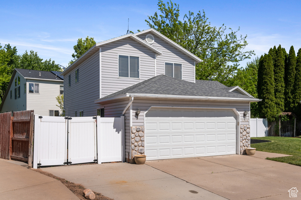 Traditional home with concrete driveway, a gate, fence, roof with shingles, and a garage