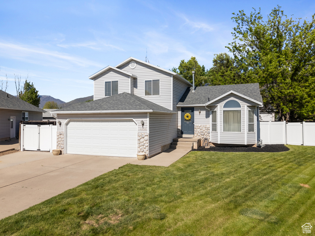 Tri-level home featuring a garage, concrete driveway, a shingled roof, and stone siding