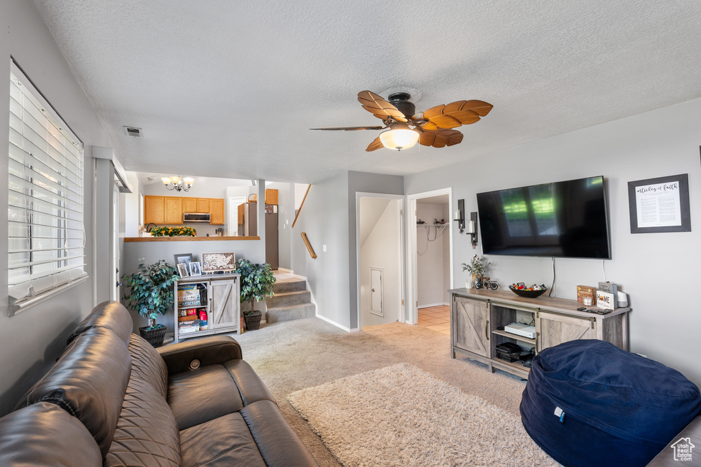 Living room with a chandelier, stairway, light colored carpet, a textured ceiling, and ceiling fan