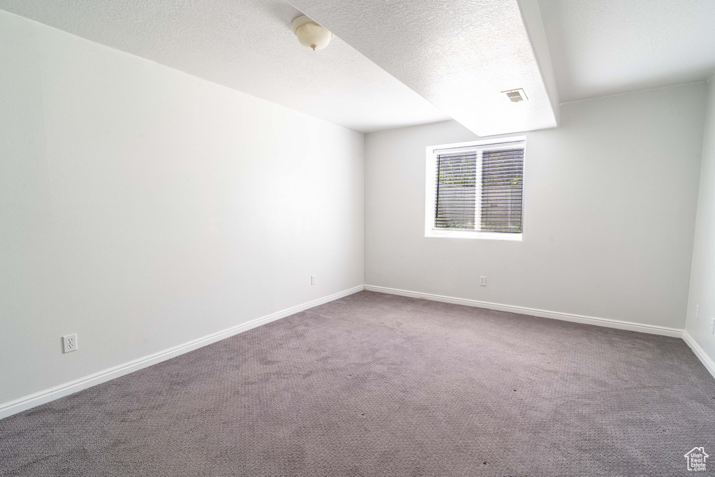 Spare room featuring carpet floors, baseboards, and a textured ceiling