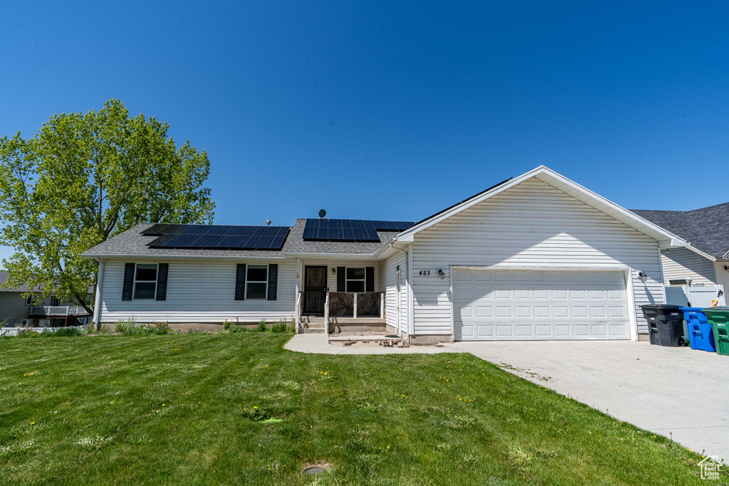 Ranch-style home featuring a garage, roof mounted solar panels, a front lawn, concrete driveway, and roof with shingles