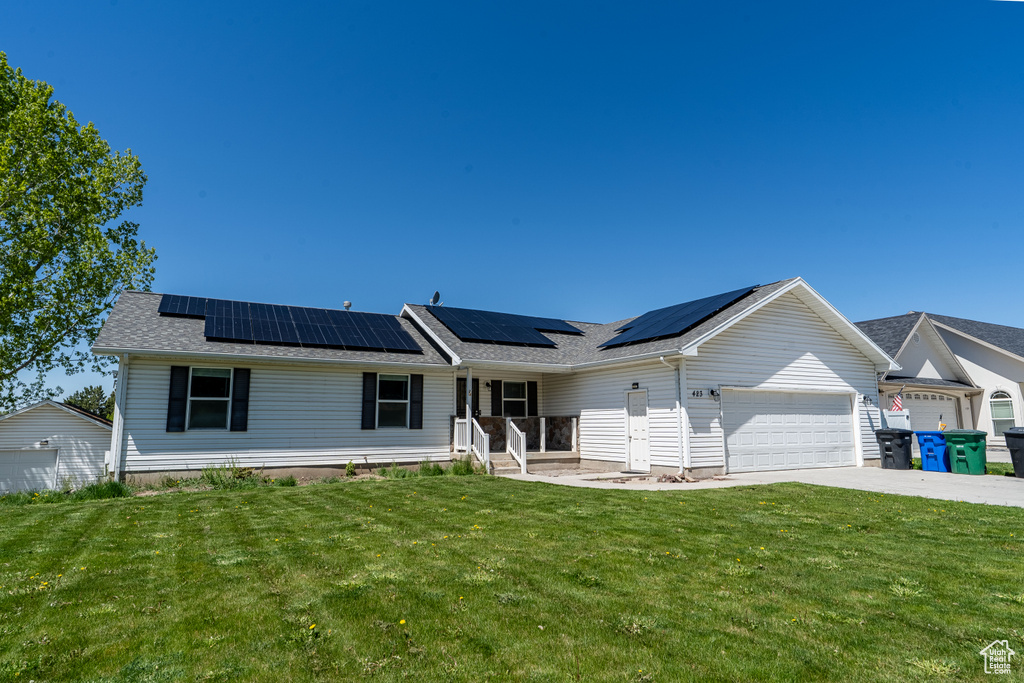 Ranch-style home with a front yard, a garage, driveway, and solar panels