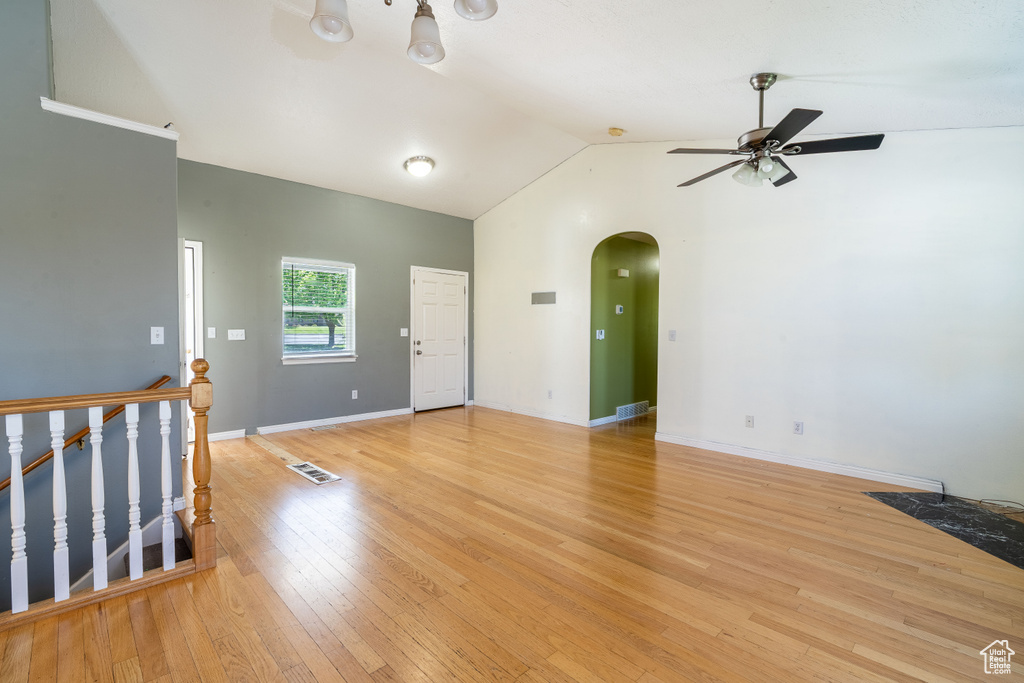 Empty room with arched walkways, ceiling fan, vaulted ceiling, light wood finished floors, and baseboards