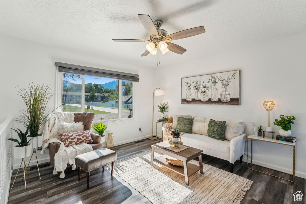 Living area with a ceiling fan, baseboards, dark wood-style floors, and a textured ceiling