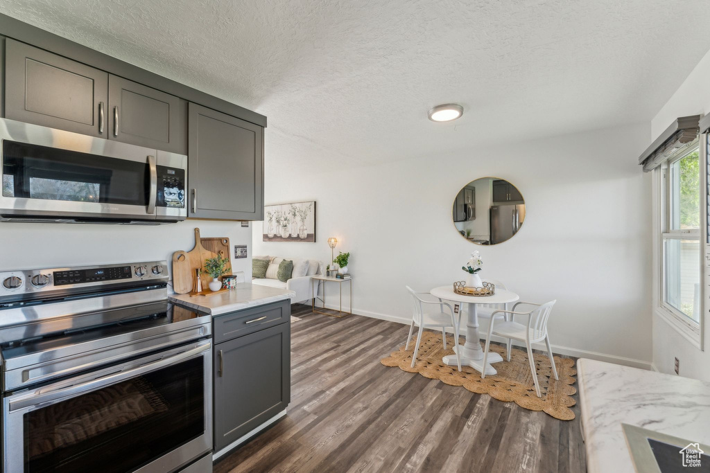 Kitchen featuring stainless steel appliances, light countertops, gray cabinetry, dark wood finished floors, and baseboards