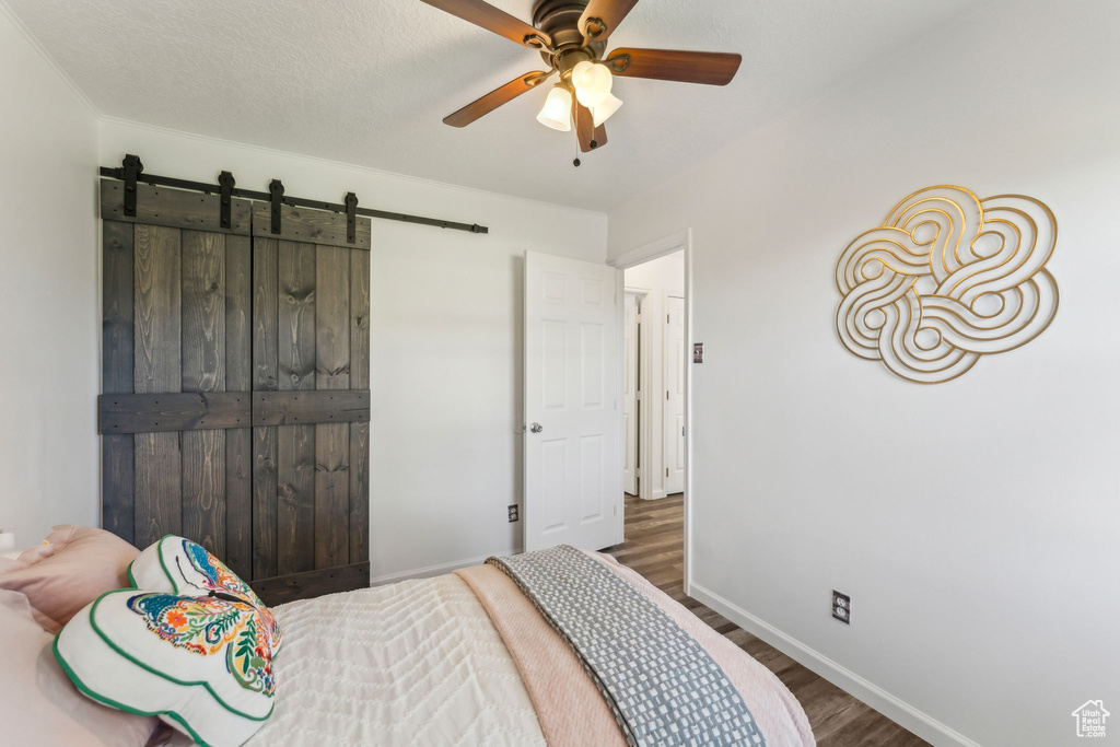 Bedroom featuring wood finished floors, baseboards, a barn door, and ceiling fan