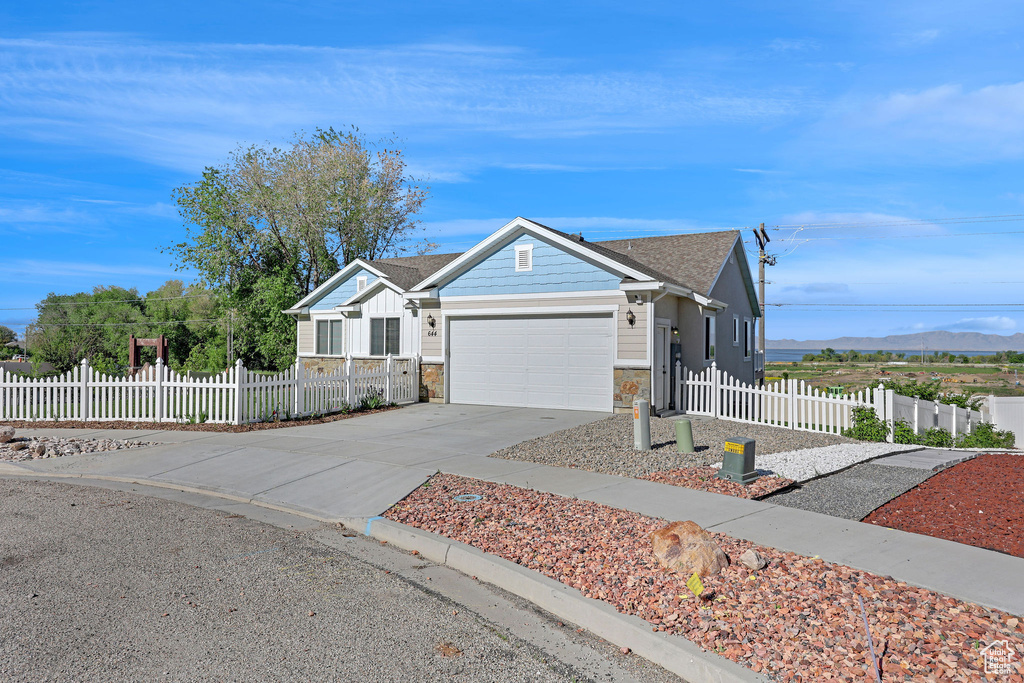 Ranch-style home featuring an attached garage, driveway, stone siding, and a fenced front yard