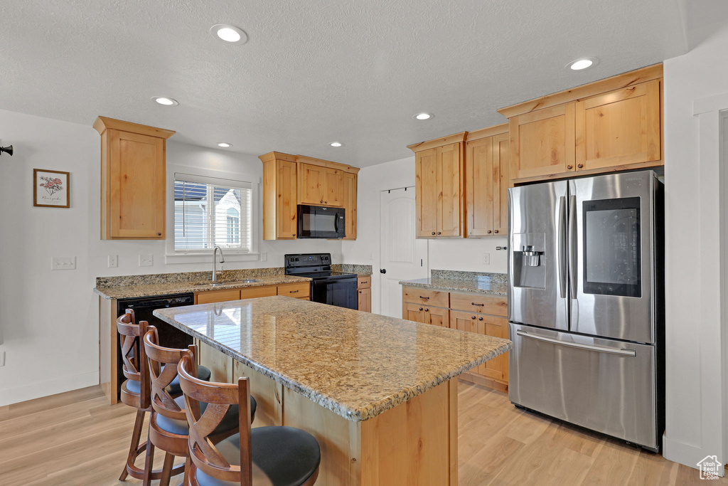 Kitchen featuring black appliances, a sink, light brown cabinets, light wood-style flooring, and a kitchen island