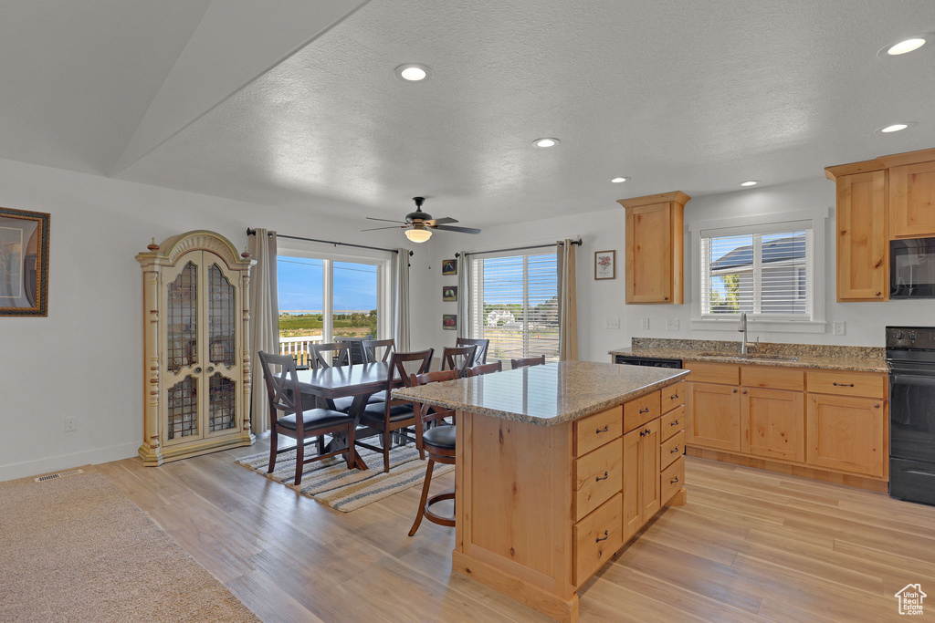 Kitchen with light brown cabinetry, a sink, stove, light wood finished floors, and a kitchen island