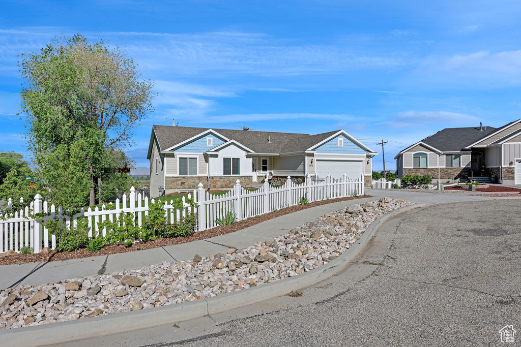 Ranch-style home featuring driveway, a fenced front yard, an attached garage, and stone siding