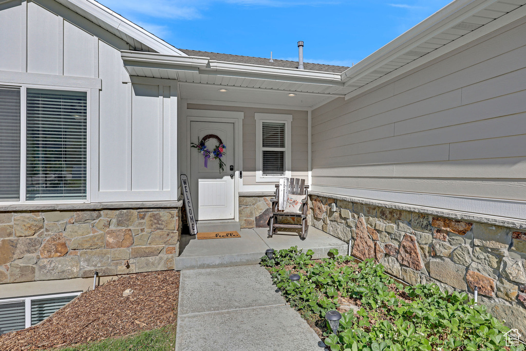Doorway to property featuring stone siding, board and batten siding, and roof with shingles