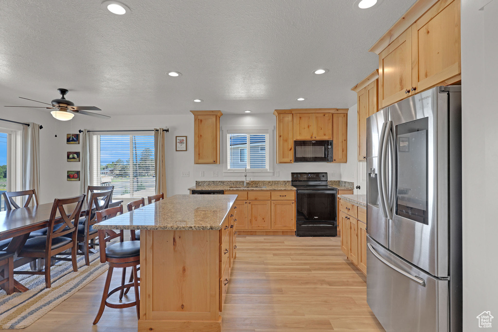 Kitchen featuring black appliances, light brown cabinets, light wood-style flooring, a sink, and a center island