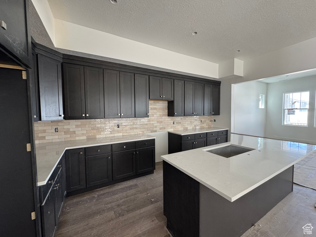 Kitchen with wood-type flooring, tasteful backsplash, a textured ceiling, and a center island