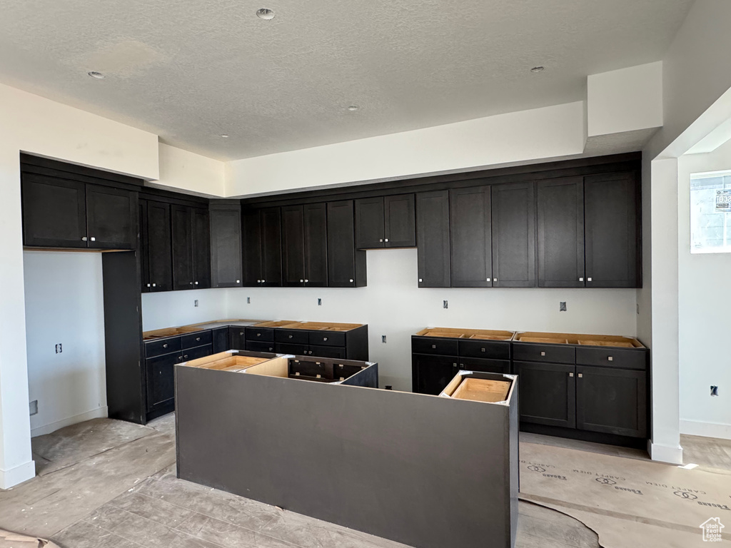 Kitchen featuring baseboards, a kitchen island, dark cabinetry, and a textured ceiling
