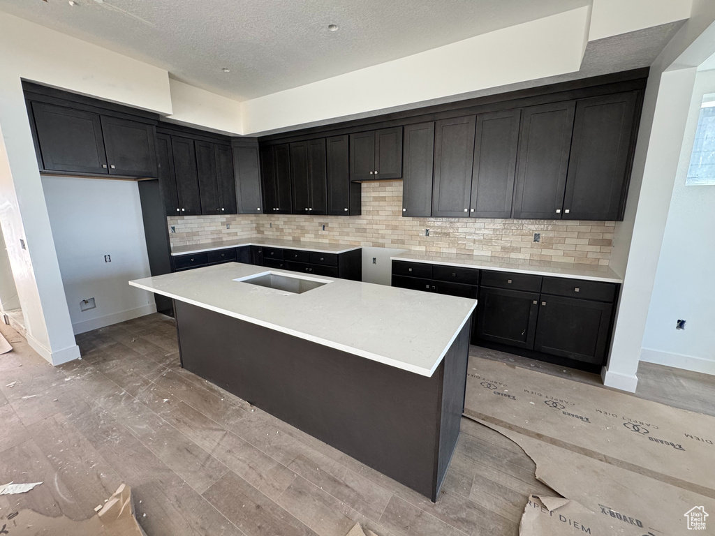 Kitchen with tasteful backsplash, a kitchen island with sink, a textured ceiling, and light wood-type flooring
