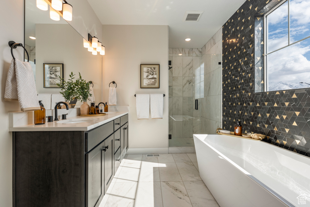 Full bathroom with baseboards, a freestanding bath, marble look tile flooring, a stall shower, and double vanity
