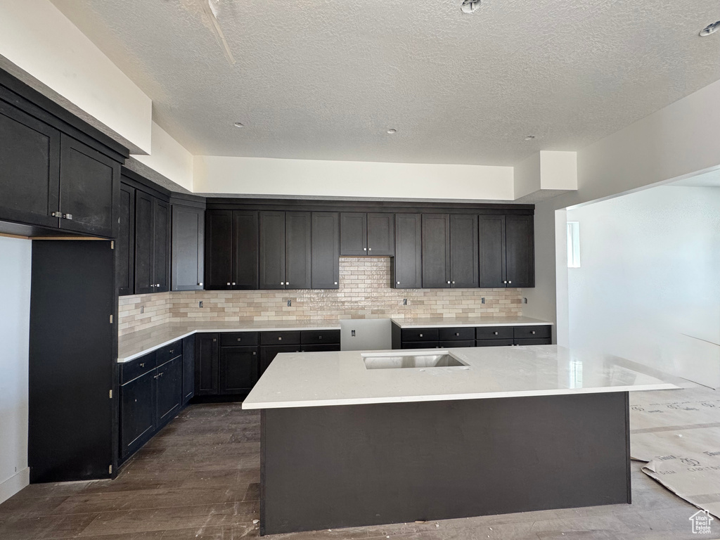 Kitchen with dark wood-type flooring, tasteful backsplash, a textured ceiling, a kitchen island, and light countertops