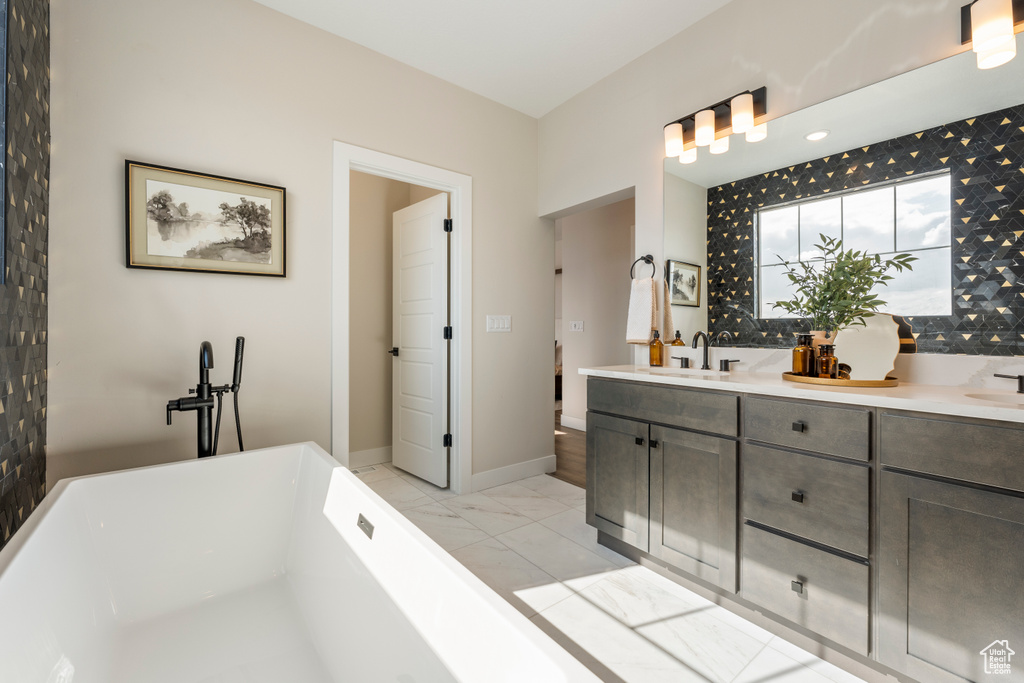 Full bathroom featuring a freestanding bath, double vanity, marble finish flooring, and baseboards