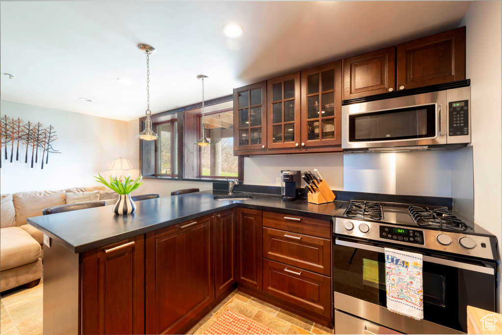 Kitchen with stainless steel appliances, a peninsula, a sink, open floor plan, and dark countertops