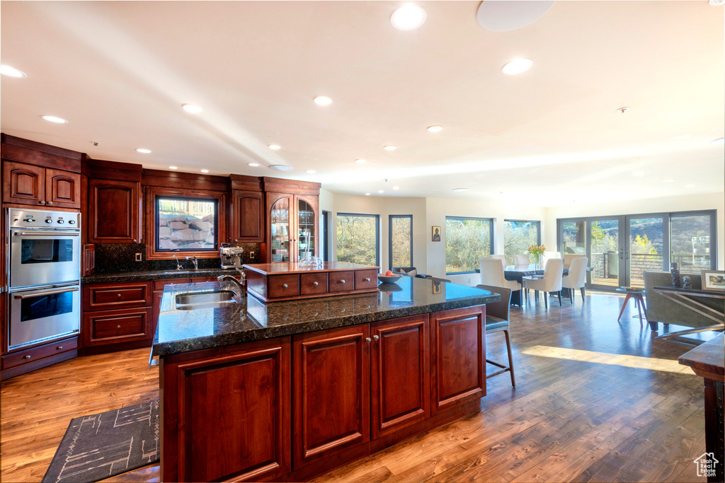 Kitchen featuring a sink, stainless steel double oven, a center island with sink, recessed lighting, and dark brown cabinets