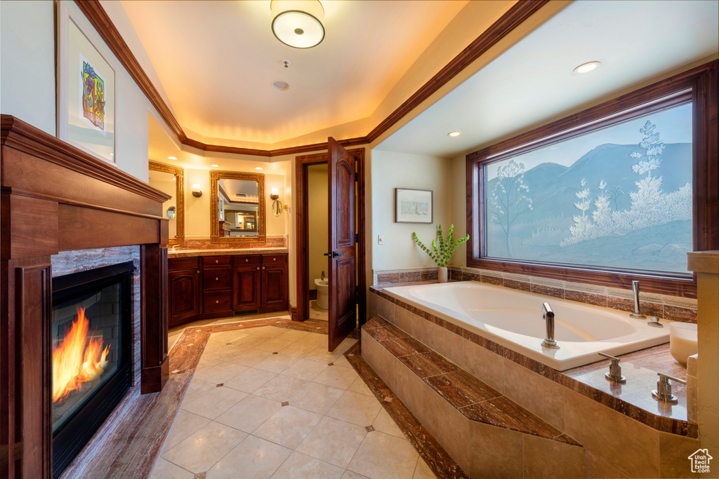 Full bathroom with a glass covered fireplace, toilet, tile patterned flooring, a garden tub, and inlaid floor details
