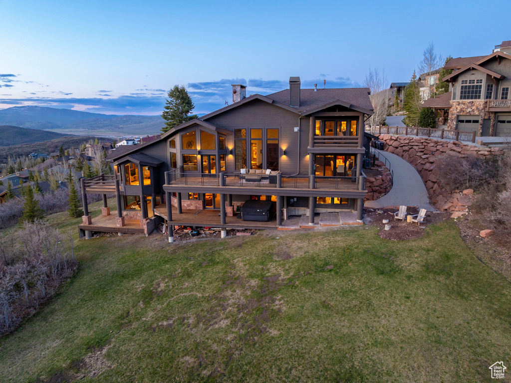 Rear view of property featuring a deck with mountain view, a lawn, a hot tub, and a chimney