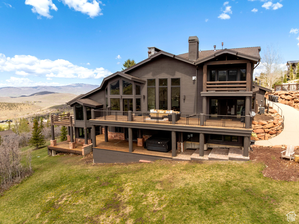 Rear view of house with a yard, a deck with mountain view, and a chimney