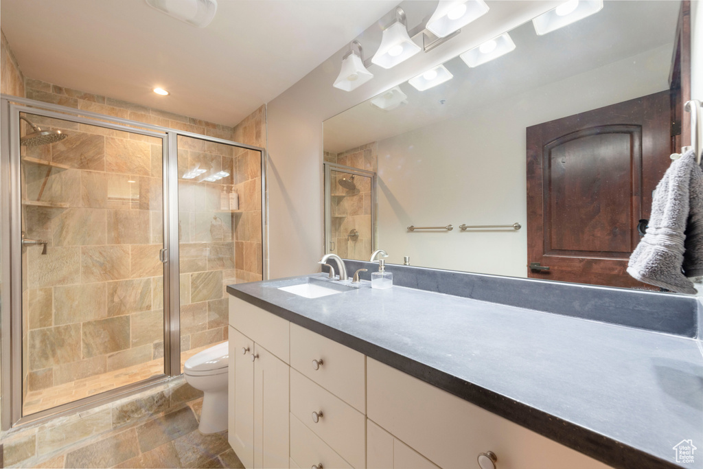 Bathroom with toilet, a stall shower, vanity, and stone finish floors