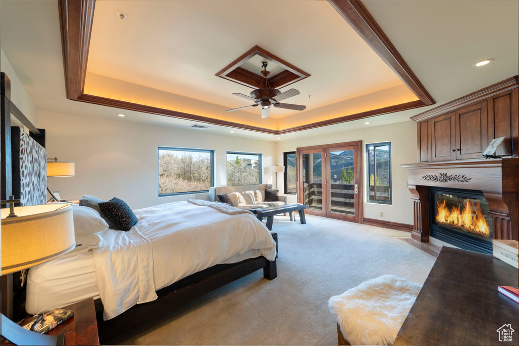 Bedroom with a tray ceiling, access to exterior, a fireplace with flush hearth, multiple windows, and recessed lighting