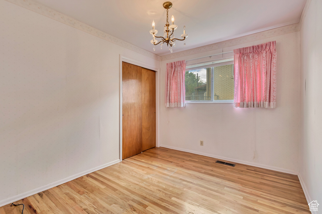 Unfurnished room with a chandelier, wood finished floors, and baseboards