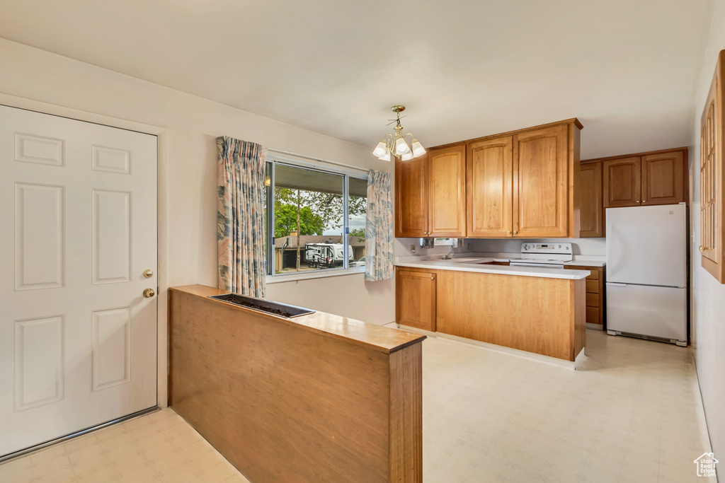 Kitchen with white appliances, light flooring, a peninsula, light countertops, and a chandelier