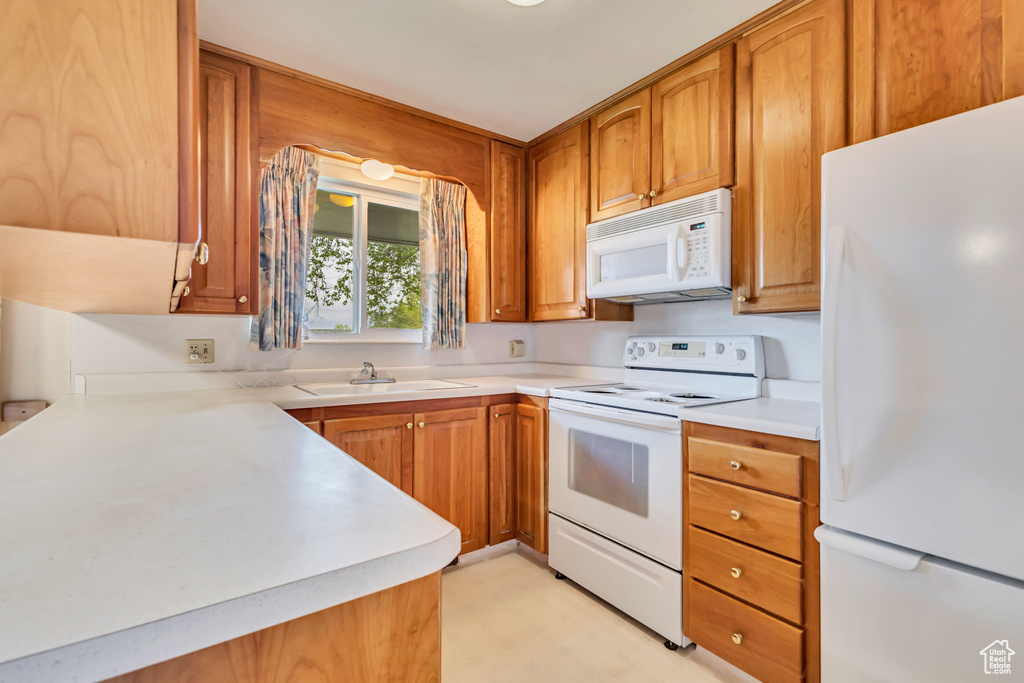 Kitchen featuring white appliances, a sink, light floors, brown cabinets, and light countertops
