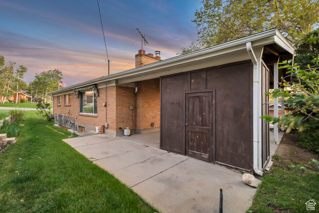 Back of house with a chimney, a lawn, brick siding, and a patio area