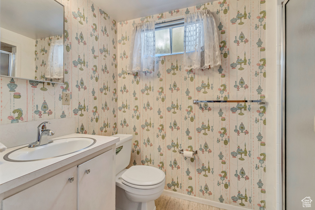 Bathroom featuring wallpapered walls, toilet, and vanity