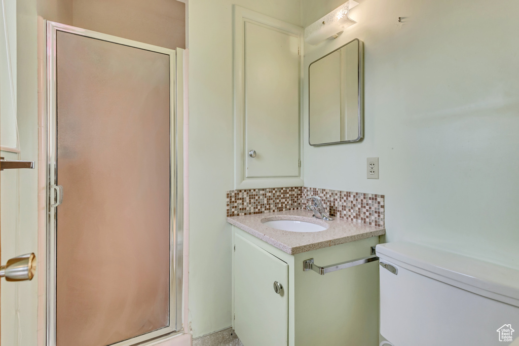Bathroom featuring a shower stall, decorative backsplash, toilet, and vanity