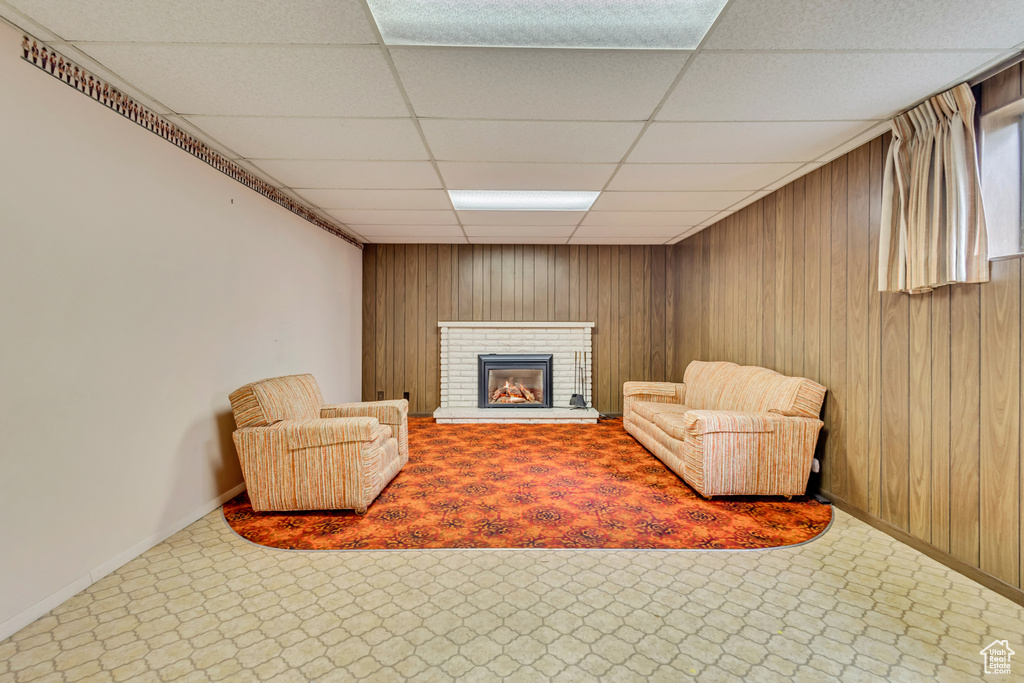 Sitting room with a drop ceiling, baseboards, wood walls, and a brick fireplace
