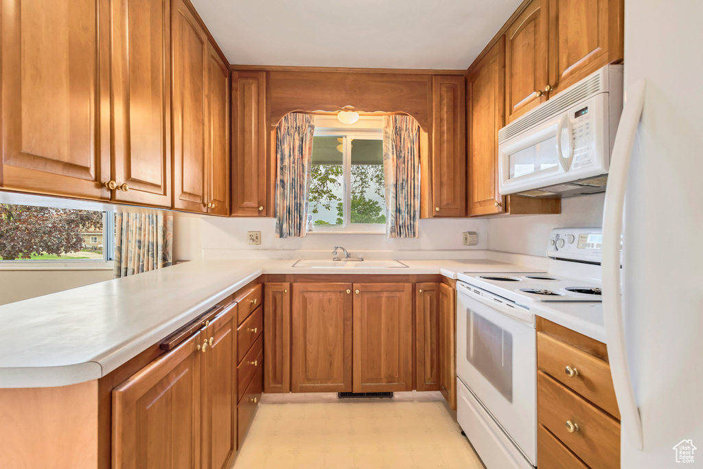 Kitchen with white appliances, a sink, light floors, and brown cabinetry