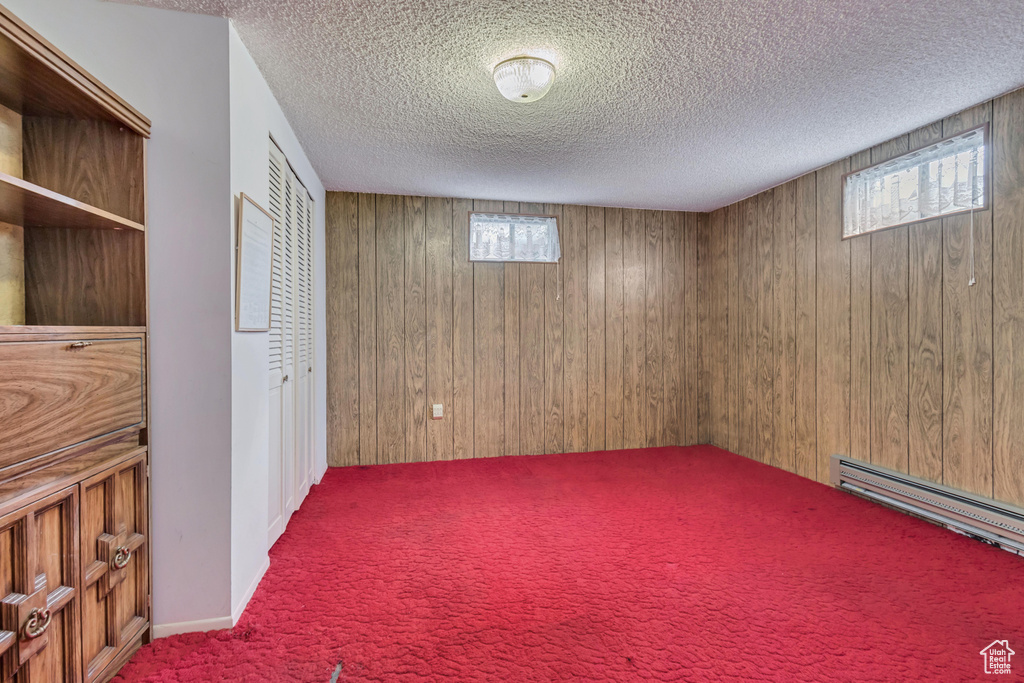 Basement with wood walls, carpet flooring, a textured ceiling, and baseboard heating