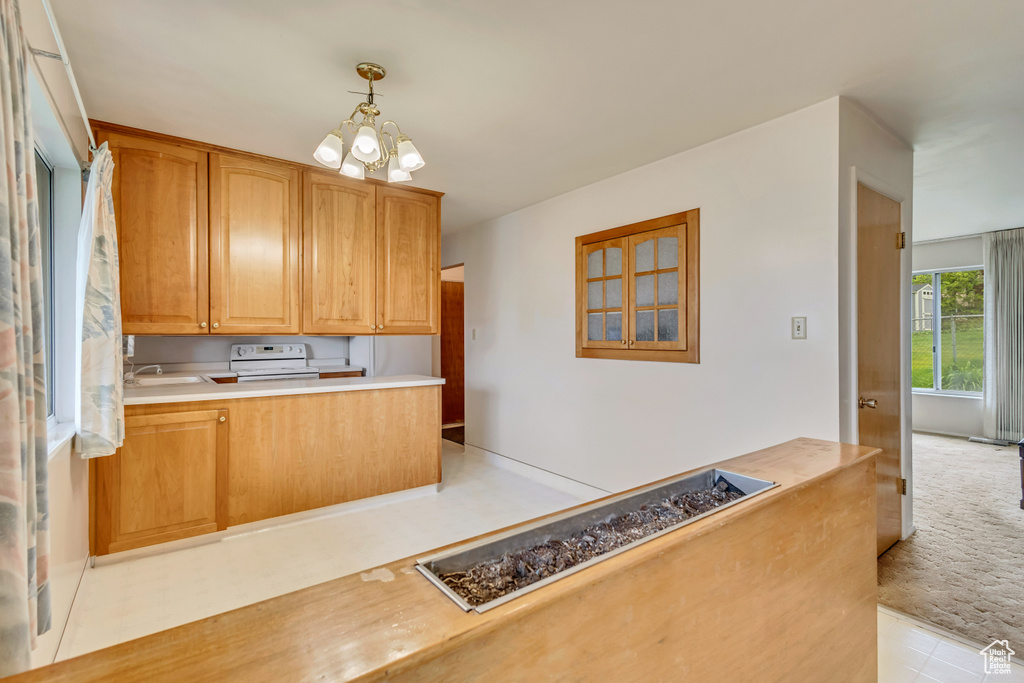 Kitchen featuring white electric stove, a sink, light countertops, a chandelier, and decorative light fixtures