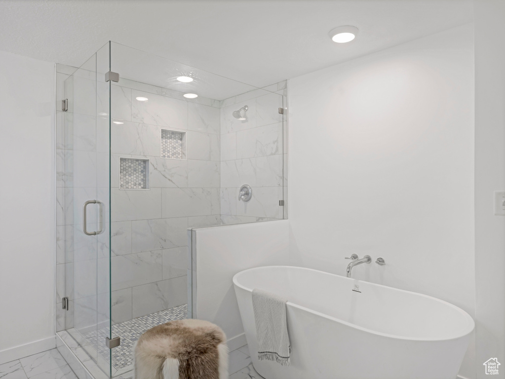Bathroom with marble finish flooring, a freestanding bath, a stall shower, and baseboards