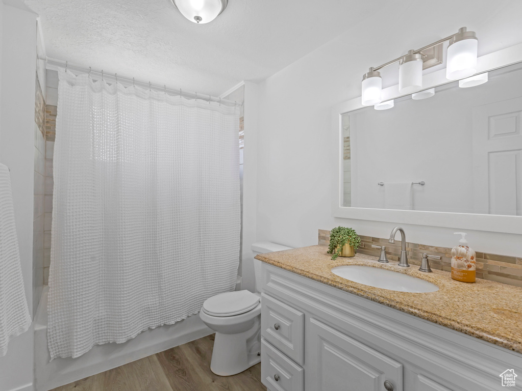 Full bathroom with toilet, shower / tub combo with curtain, vanity, and wood finished floors