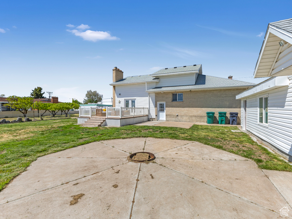 Back of property with a patio, a lawn, a deck, brick siding, and roof with shingles