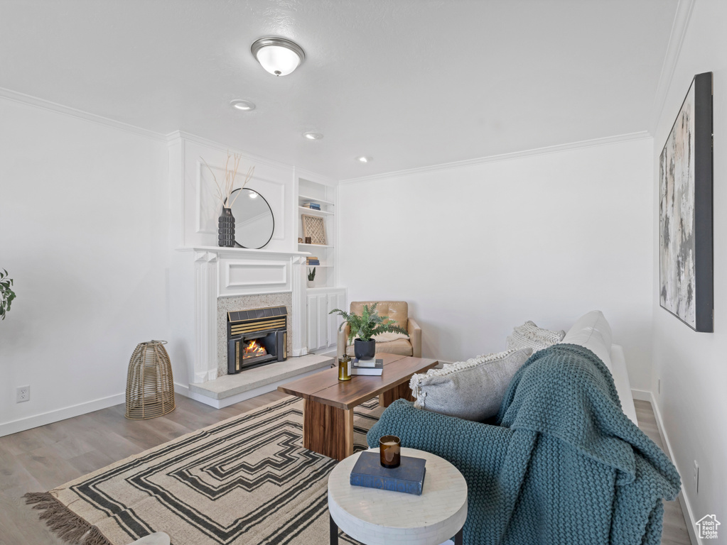 Living room featuring wood finished floors, baseboards, crown molding, a premium fireplace, and built in shelves