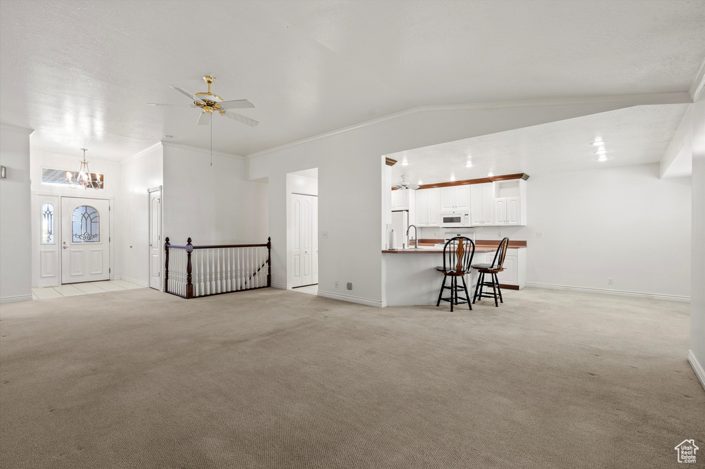 Unfurnished living room with light carpet, a chandelier, ceiling fan, crown molding, and baseboards